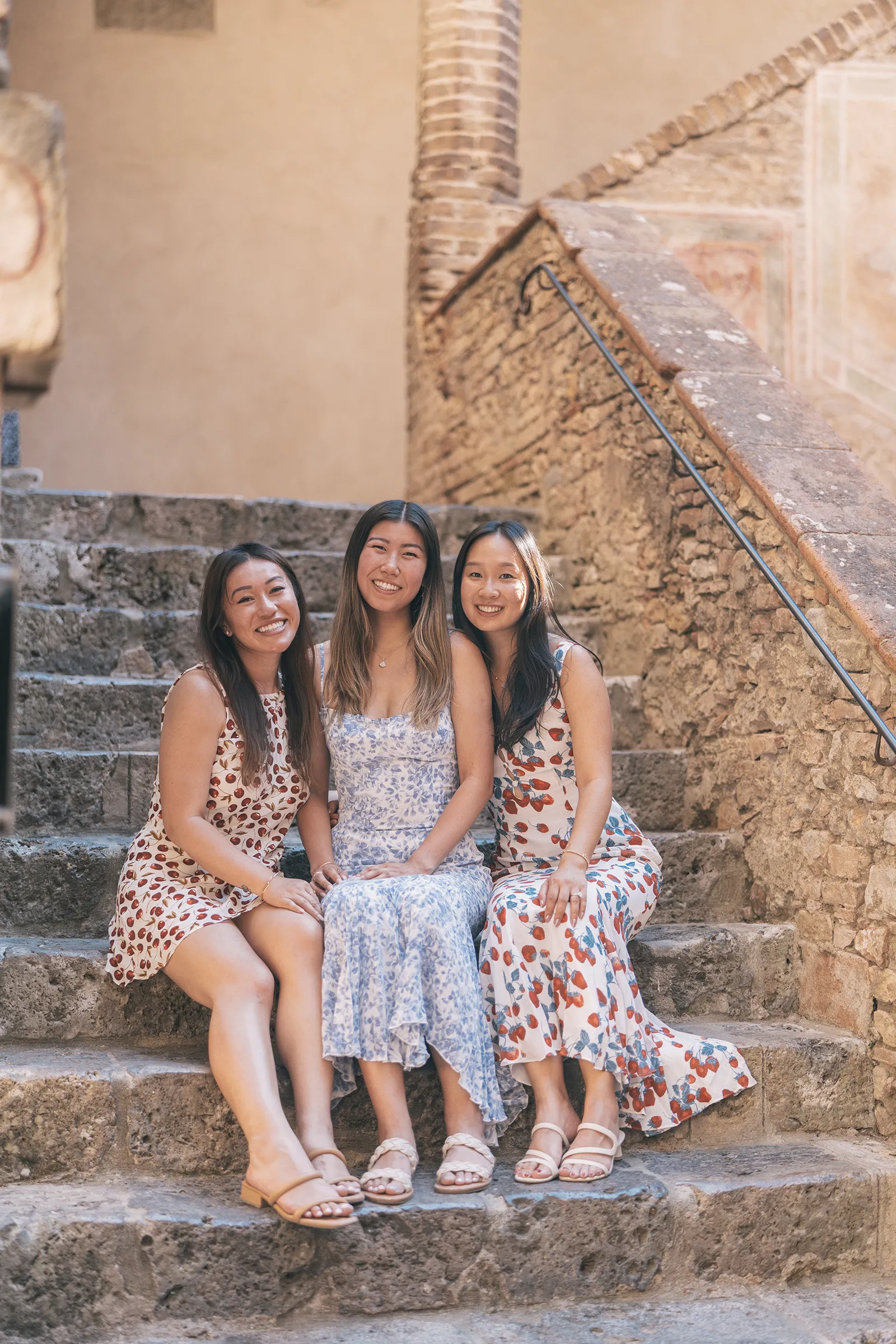 Three friends standing at a stone wall overlooking the rolling hills of Tuscany during a girls trip photoshoot.