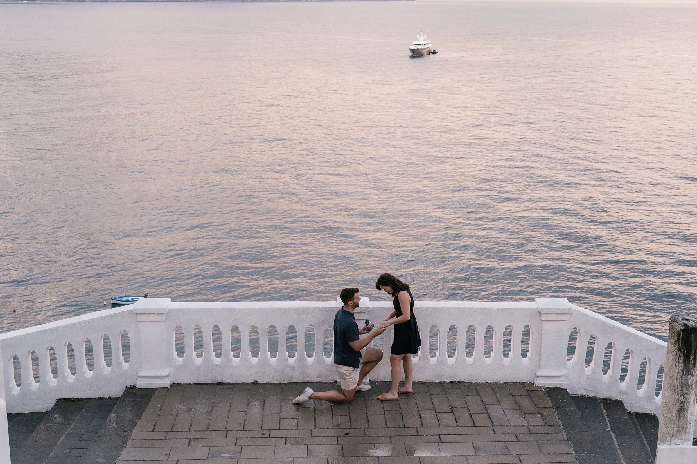 Man kneeling to propose on a white terrace overlooking the sea at sunset